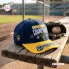 Front view of a blue and yellow Milwaukee Brewers snapback cap resting on a wooden bench near a baseball glove.