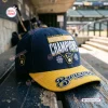 Side angle of the Milwaukee Brewers 2026 National League Champions Snapback Cap resting on a wooden bench.