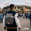 Rear view of a person wearing the Milwaukee Brewers 2026 World Series Champions Baseball Jacket outside a stadium.