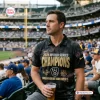 Man wearing Milwaukee Brewers 2026 World Series Champions polo shirt at a stadium holding a drink.