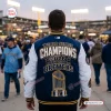 Back view of a fan wearing a blue and white Milwaukee Brewers World Series Champions varsity jacket at a stadium.