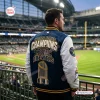 Rear view of a fan wearing a blue and white Milwaukee Brewers World Series Champions varsity jacket at a stadium.