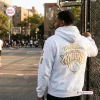 Back view of a person wearing a New York Knicks white hoodie with gold championship graphics on an outdoor basketball court.