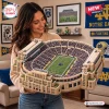 A smiling woman holding a detailed Notre Dame Fighting Irish plush stadium pillow in a decorated room.