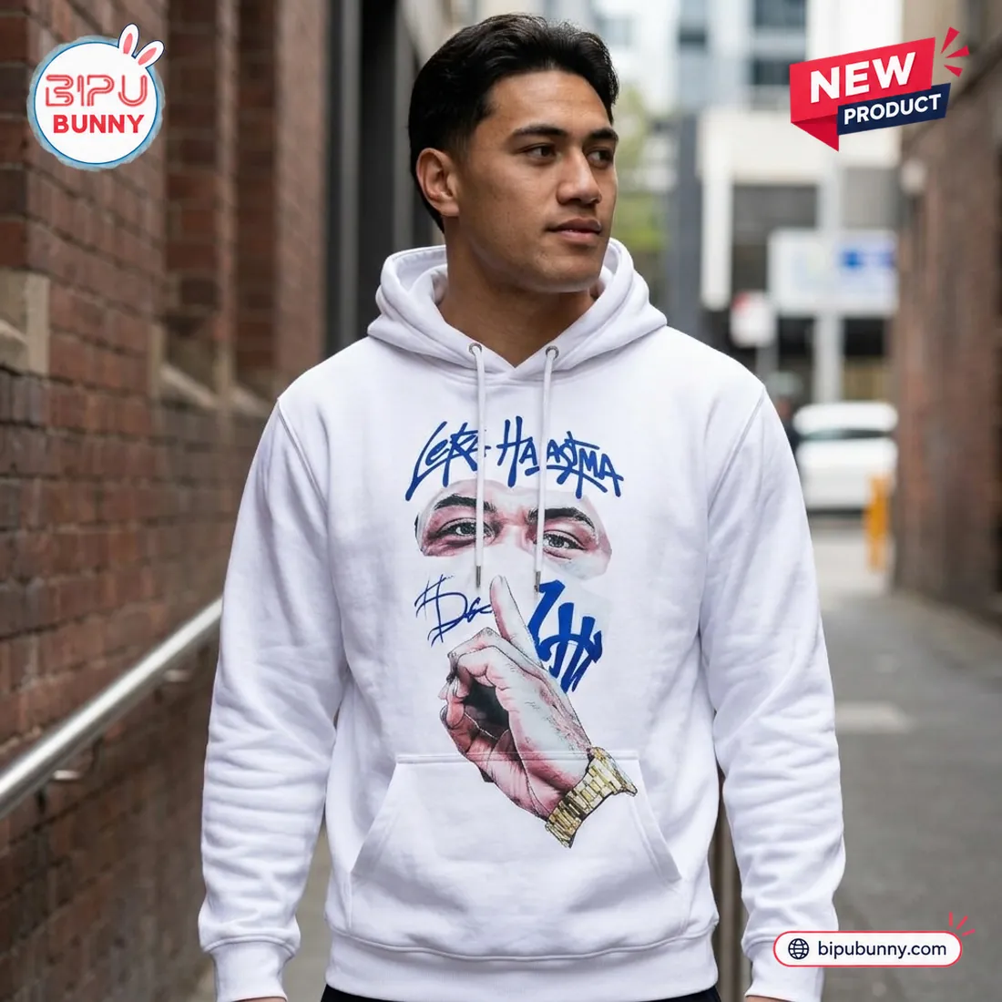 Man wearing the white NZ Warriors Leka Halasima Limited Edition Hoodie in a brick alleyway showing the front shush portrait and royal-blue graffiti lettering
