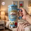 Hand holding a blue tie-dye YETI Handle Tumbler featuring Peanuts 77th Anniversary graphics.