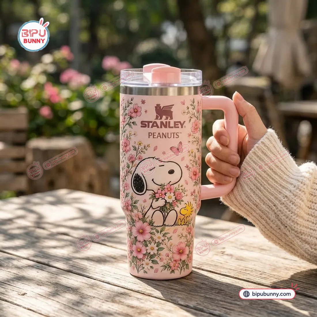 In-hand outdoor view of the Peanuts Flora 40oz Tumbler Cup showing Snoopy, Woodstock, and the pastel pink handle