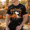 Front view of a black t-shirt featuring a Peanuts Great Pumpkin 60th Anniversary graphic with Snoopy and autumn leaves.