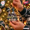 Closeup of hands hanging a football play figurine ornament on a lit Christmas tree.