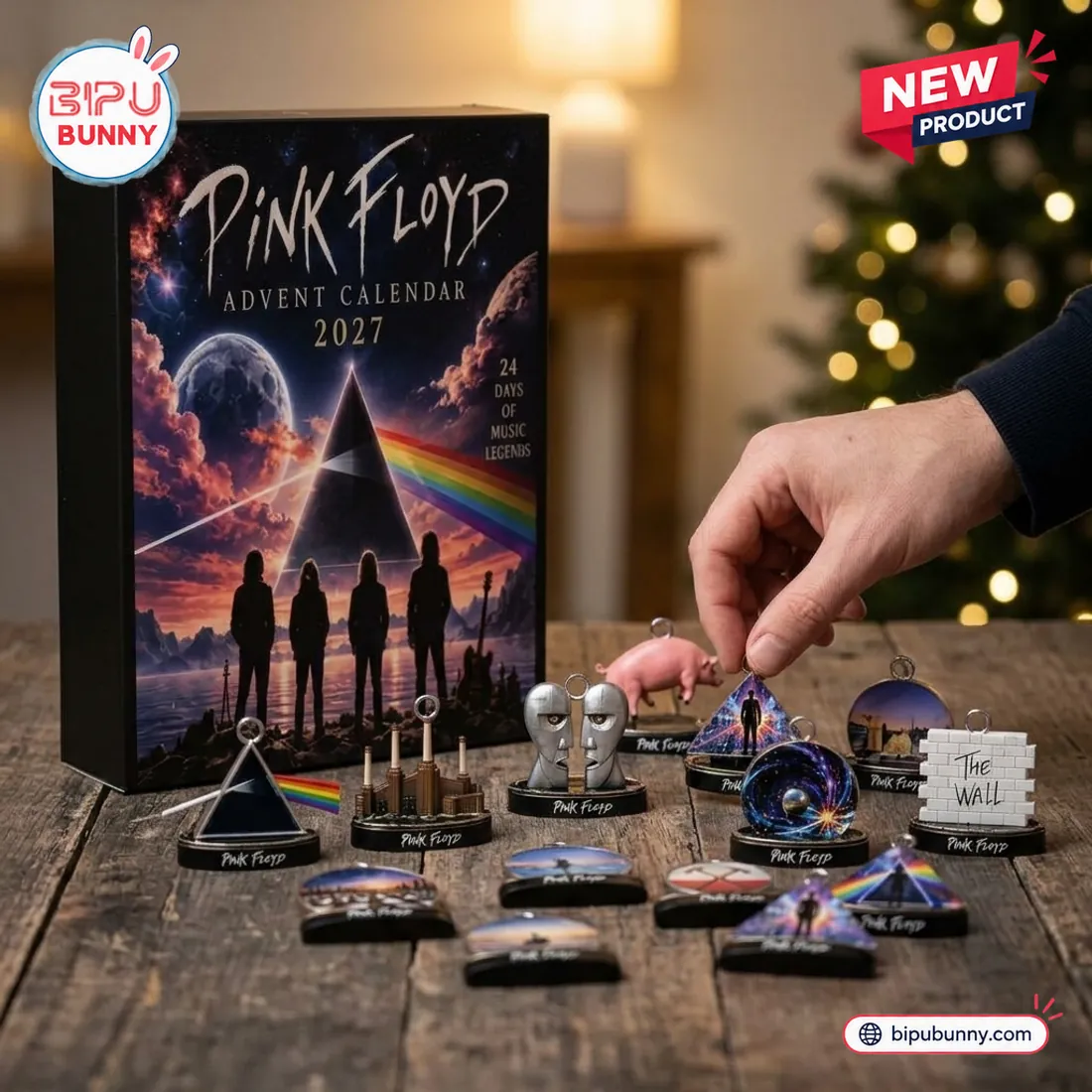 Hand holding a Pink Floyd prism ornament above the flat-base Battersea Power Station, Division Bell heads, and The Wall miniatures on a wooden table