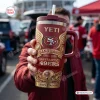 Close-up of a San Francisco 49ers 80th Anniversary stainless steel tumbler with handle held outdoors.