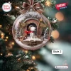 Close-up view of a clear holiday snow globe ornament hanging on a pine tree branch with a flying character figure inside.