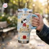 Hand holding Snoopy Joe Cool handle tumbler outdoors with blue sky and cloud pattern.