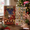 Front view of the Snoopy Peanuts Gang 2026 Advent Calendar box alongside a plastic tray with holiday-themed character charms.
