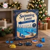 Front view of the Swimming Lover Advent Calendar 2026 box with swimming-themed acrylic charms on a wooden table.