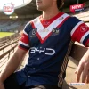 Close-up of a person wearing the Sydney Roosters 2026 NRL Premiers Baseball Jersey seated at a stadium.