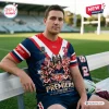 Man wearing the Sydney Roosters 2026 NRL Premiership Shirt while sitting on a bench at a sports field.