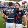 Back view of rugby players embracing in dark blue Sydney Roosters 2026 Premiers jerseys on field.