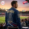 Back view of a man wearing a blue Sydney Roosters 2026 Premiers Varsity Jacket at a stadium.