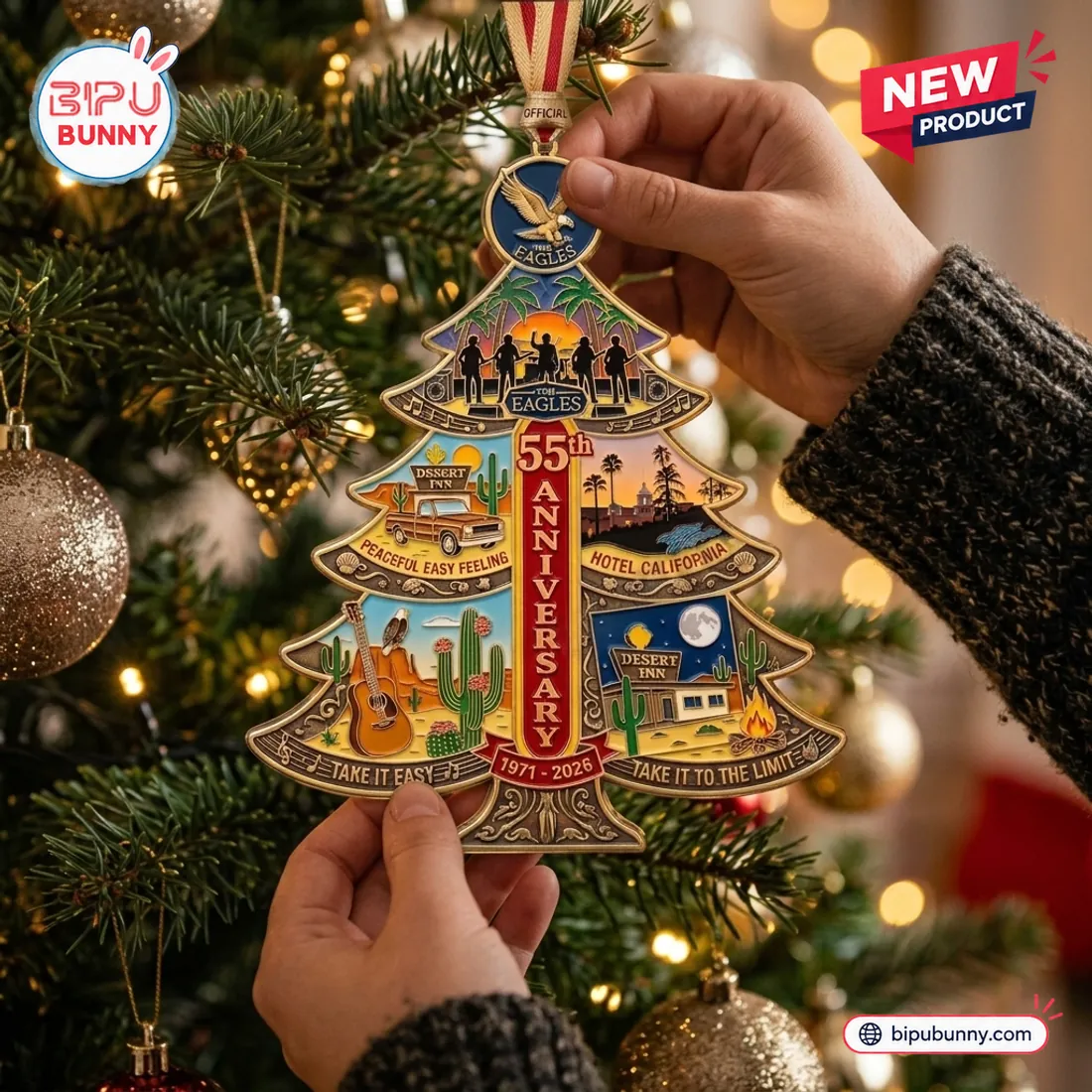 Hands hanging The Eagles 55th Anniversary Christmas Ornament on a pine branch, highlighting the top bald eagle medallion and five-member sunset stage silhouette