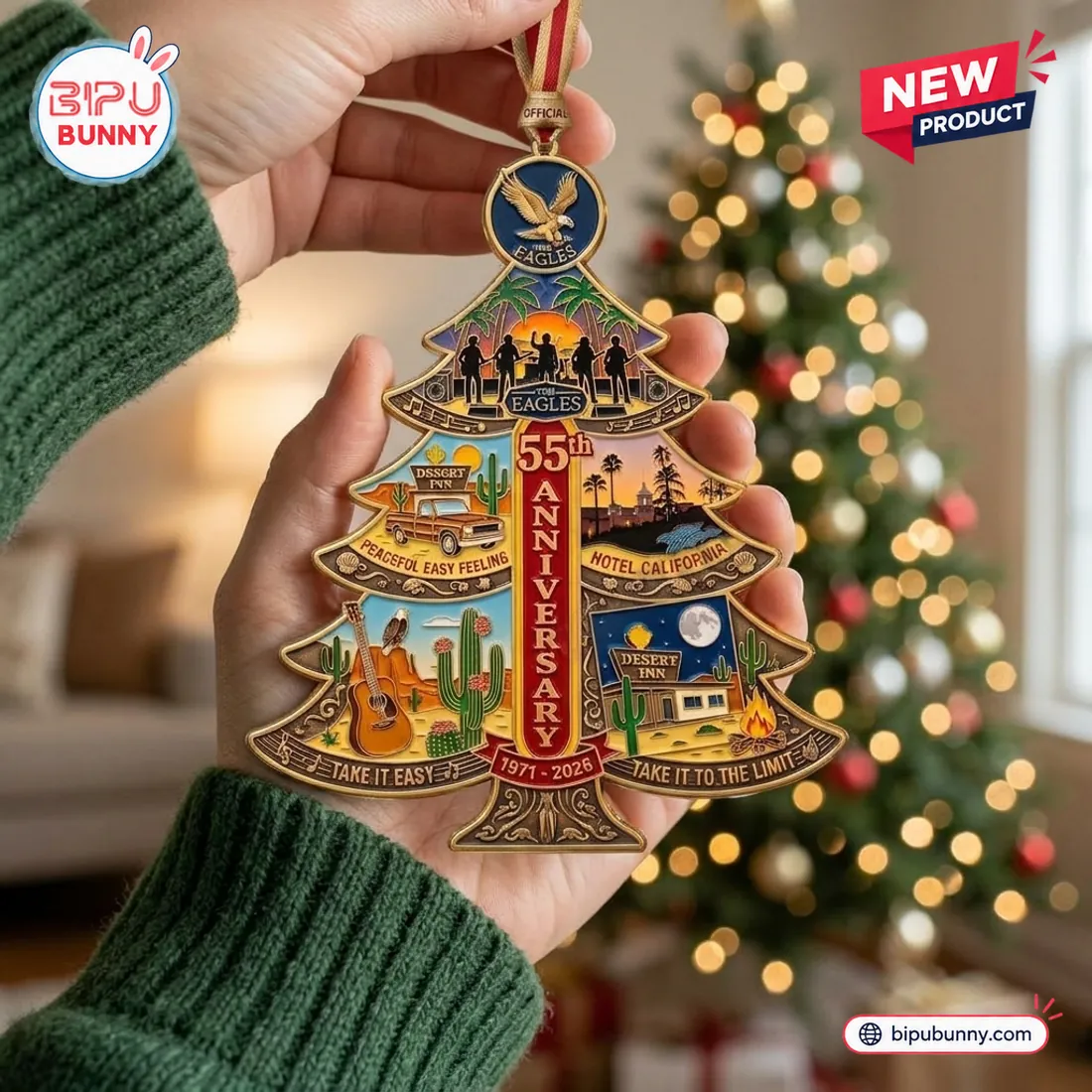 Close-up of The Eagles 55th Anniversary Christmas Ornament held in hands, showing the pre-attached cream-and-red striped satin ribbon and OFFICIAL gold clasp