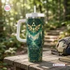 Front view of The Legend of Zelda 40th Anniversary Tumbler with green forest and gold crest on wooden table.