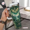 Hand holding a green The Legend of Zelda 40th Anniversary Tumbler with gold crest and forest scenery.
