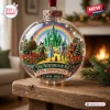 Front view of The Wizard Of Oz 87th Anniversary Glass Ornament sitting on a wooden surface.