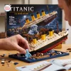 Close-up view of hands assembling the Titanic Sinking Ship Model Building Block Set with minifigures on a blue base.