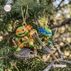 Close-up view of two TMNT Chibi Sewer Squad Advent Calendar character ornaments hanging on pine tree branches.