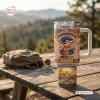 Front view of a US 250th Anniversary 1776-2026 Tumbler with handle on a wooden picnic table outdoors.