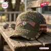 Front view of an olive green US Marine Veteran embroidered baseball cap resting on a wooden table.