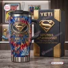 Front view of YETI Superman 88th Anniversary handle tumbler beside matching collector box.