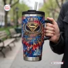 Close-up of a YETI Superman 88th Anniversary Handle Tumbler held outdoors near park benches.
