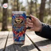 Hand holding a YETI Superman 88th Anniversary Handle Tumbler on a wooden table outdoors.