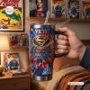 Hand holding YETI Superman 88th Anniversary Handle Tumbler with comic book background.