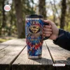 Hand holding a YETI Superman 88th Anniversary Handle Tumbler on an outdoor wooden table.